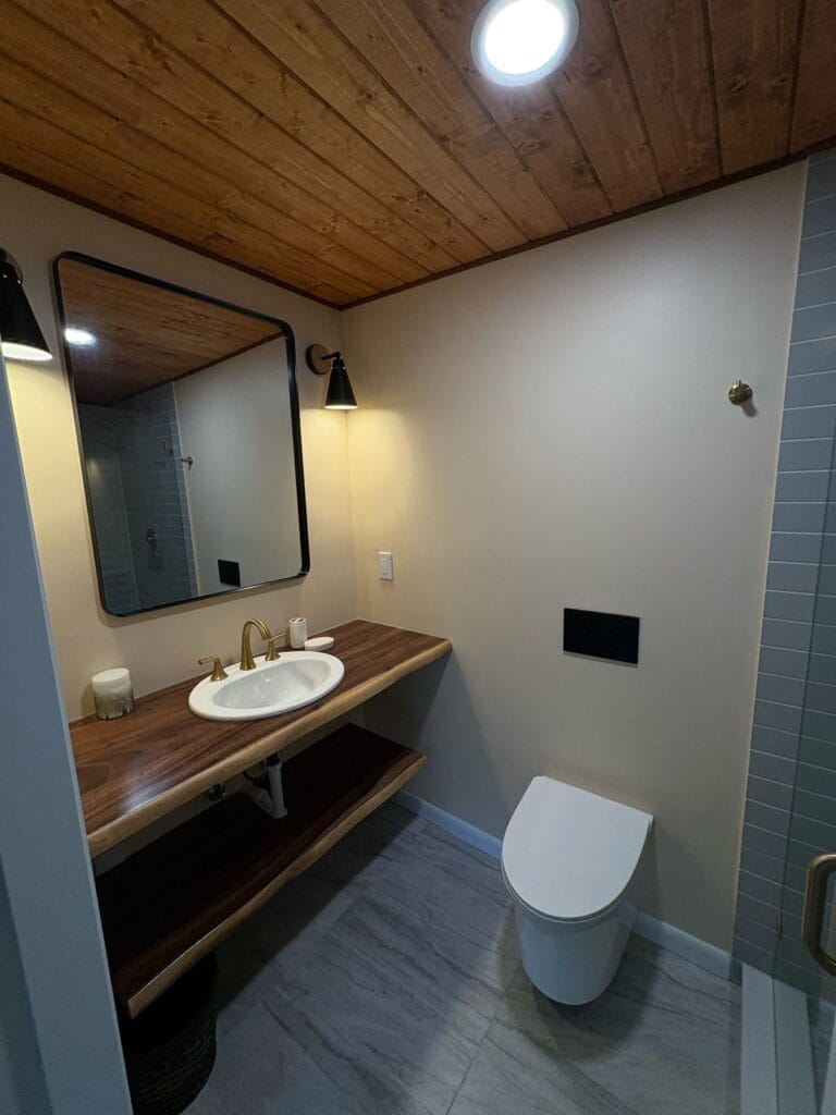 Bathroom with wood plank ceiling, black sconces, and floating live-edge vanity