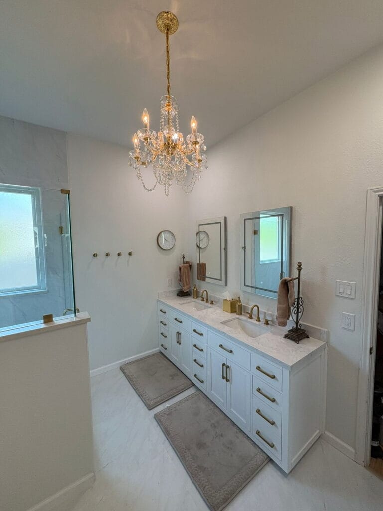 Crystal chandelier over white double vanity with gold fixtures